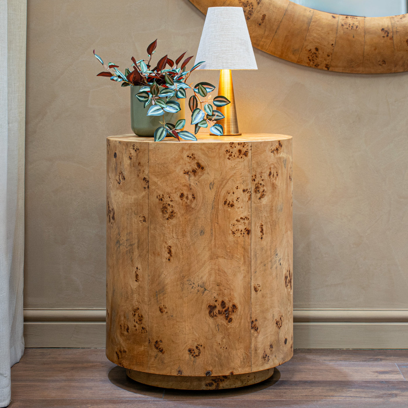 Burl-wood drum side table beneath a gold mirror — Conpanna Living